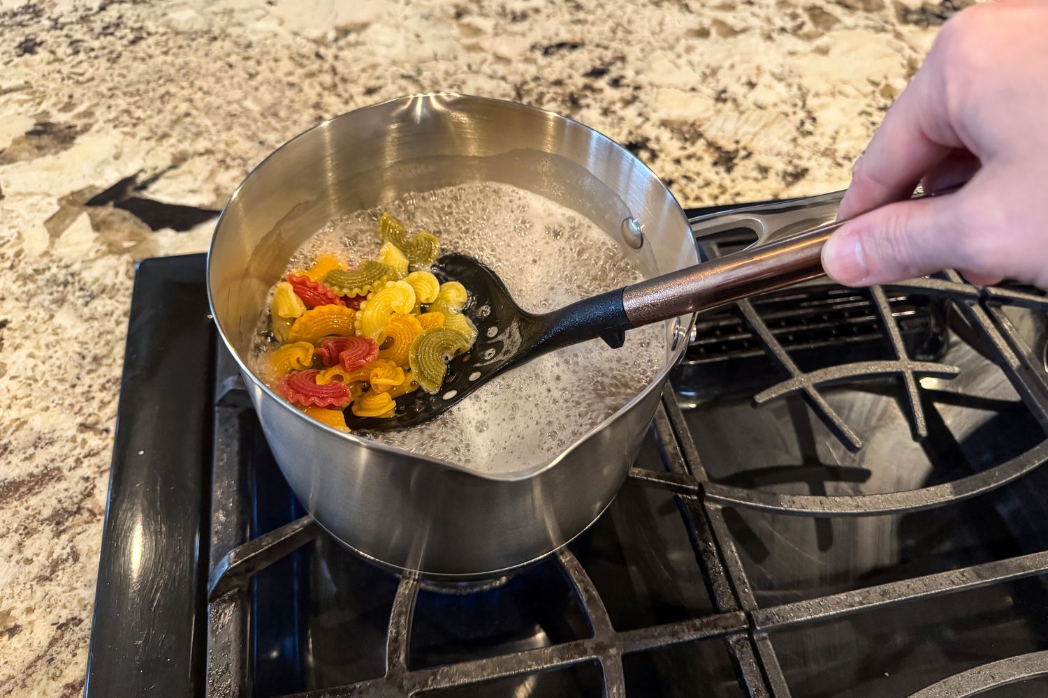 A person cooks pasta in the KitchenAid 11 Piece 3-Ply Stainless Steel Cookware Set pot