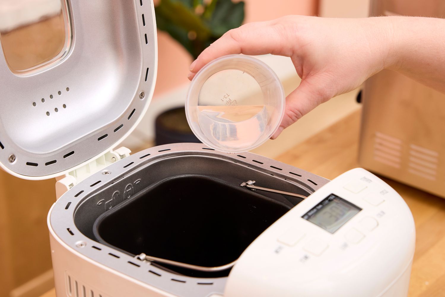 A person pours water into the Amazon Basics 2-Pound Nonstick Bread Making Machine