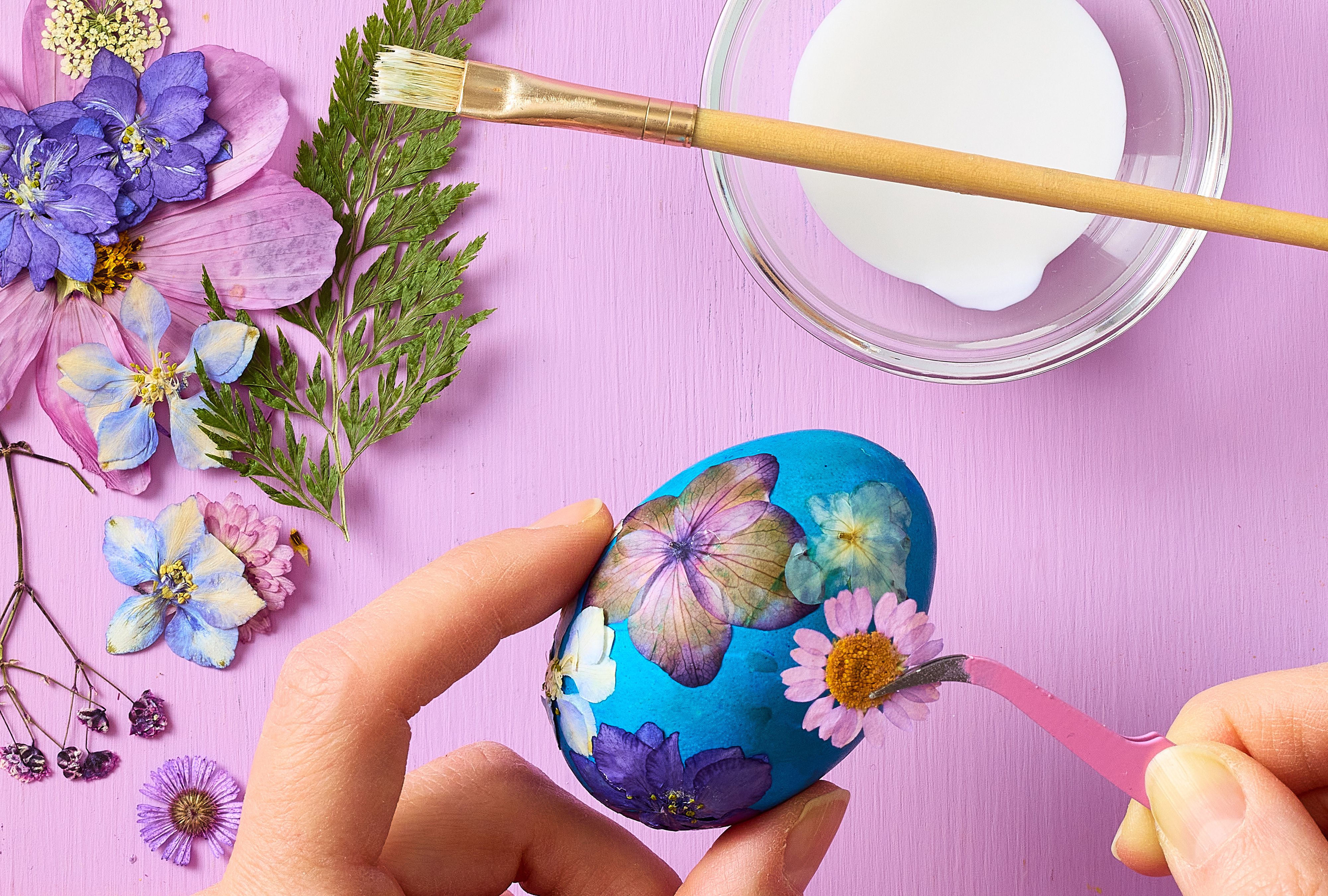 Hands holding an easter egg, and applying a flower with glue on the egg. 