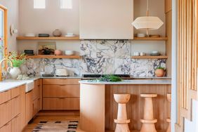 A modern kitchen interior with wooden cabinetry, marble backsplash, open shelves, and an island with stool seating
