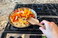 A person cooks peppers and onions in a KitchenAid 11 Piece 3-Ply Stainless Steel Cookware Set pan