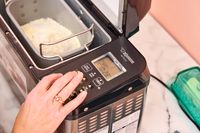 A person presses a button on the Zojirushi Home Bakery Virtuoso Plus Bread Maker