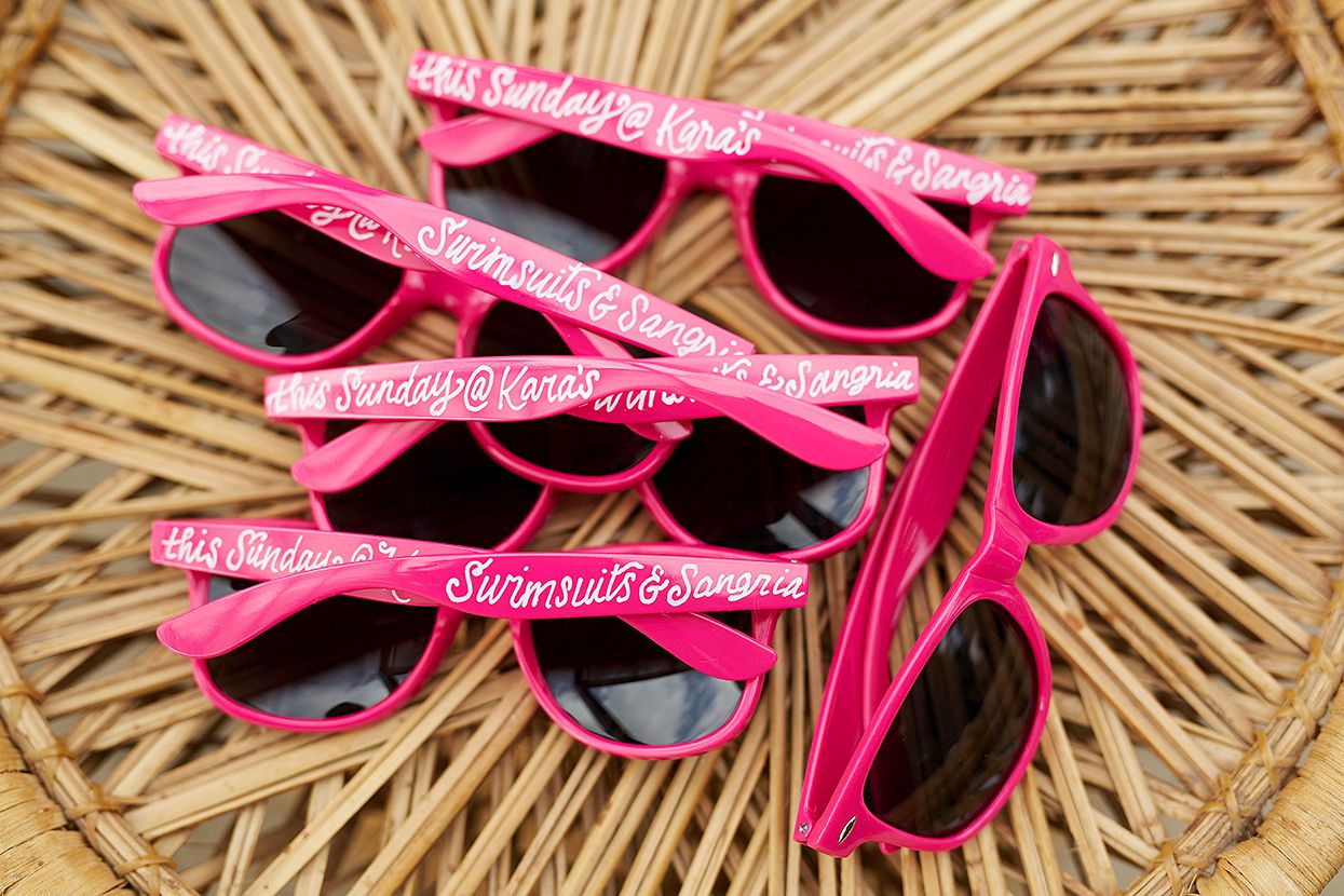 pink sunglasses with script on rattan table