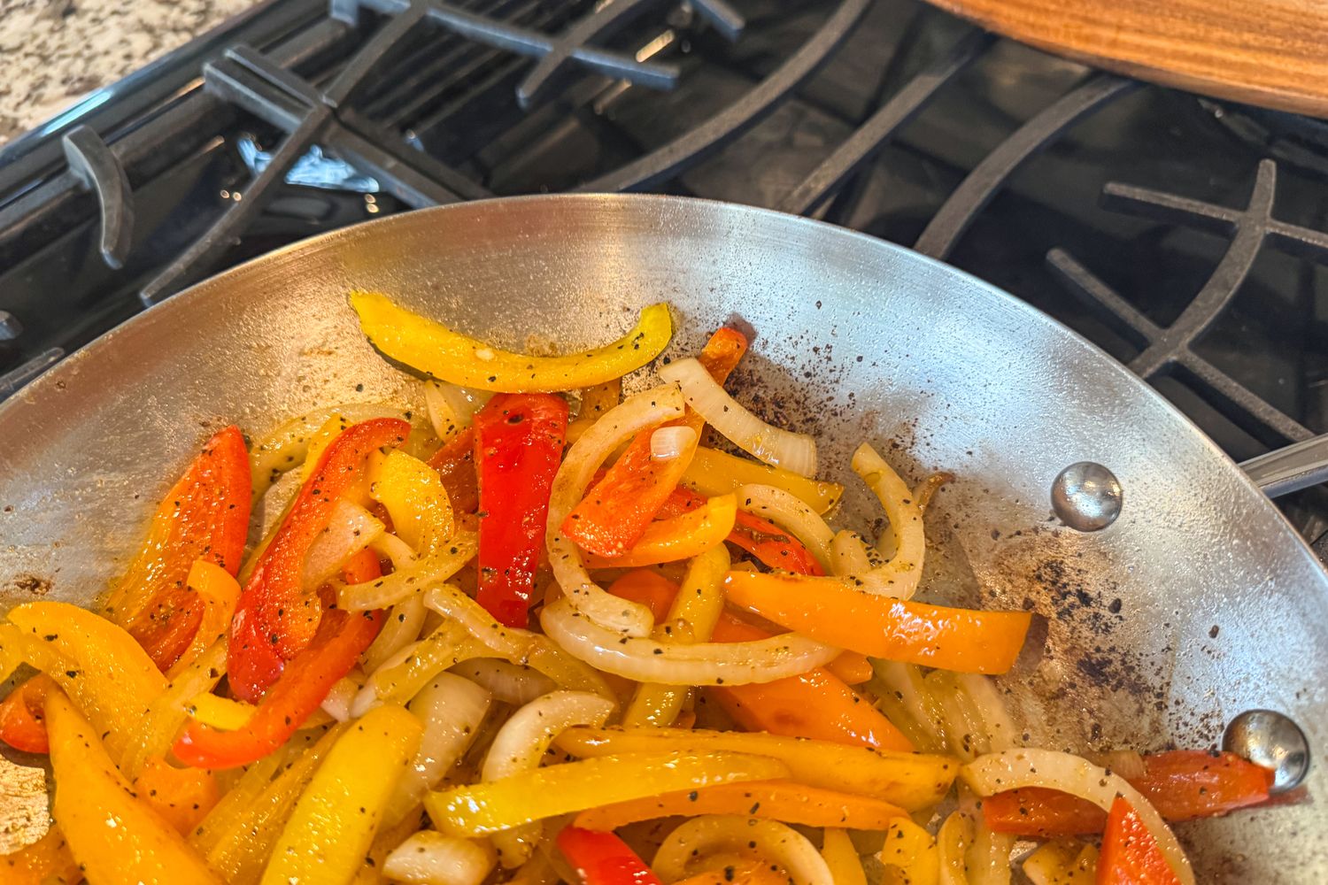 A close-up of peppers and onions cooked in the KitchenAid 11 Piece 3-Ply Stainless Steel Cookware Set pan