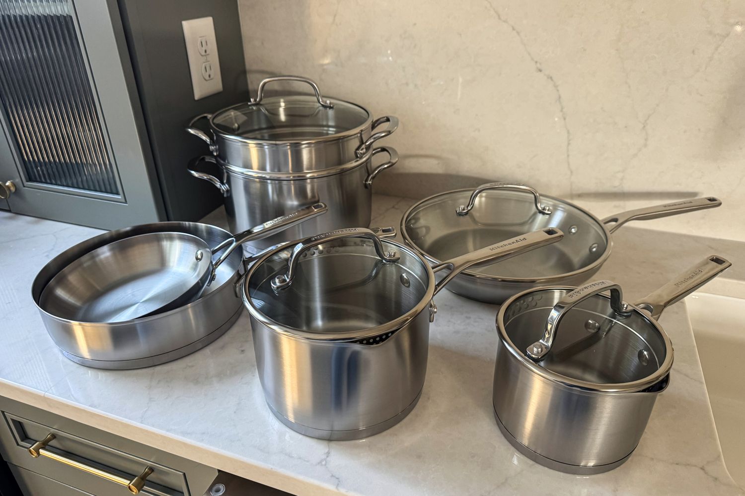The KitchenAid 11 Piece 3-Ply Stainless Steel Cookware Set on a kitchen countertop
