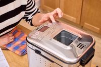 A person presses a button on the Cuisinart CBK-110 Compact Automatic Bread Maker
