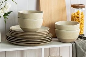 Stacked plates and bowls on a shelf with a jar of pasta and a cutting board in the background