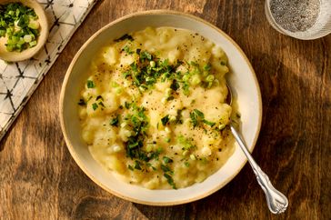 A bowl of stewed potatoes garnished with herbs on a wooden table