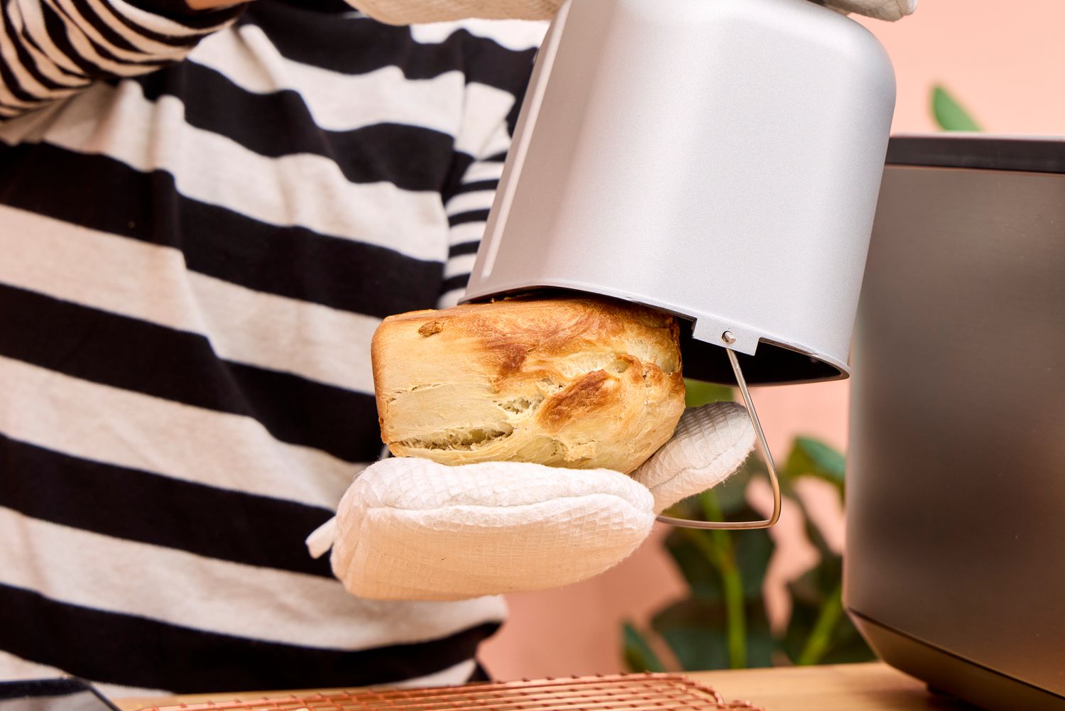 A person removes a loaf of bread from the Panasonic SD-R2550 Automatic Bread Maker