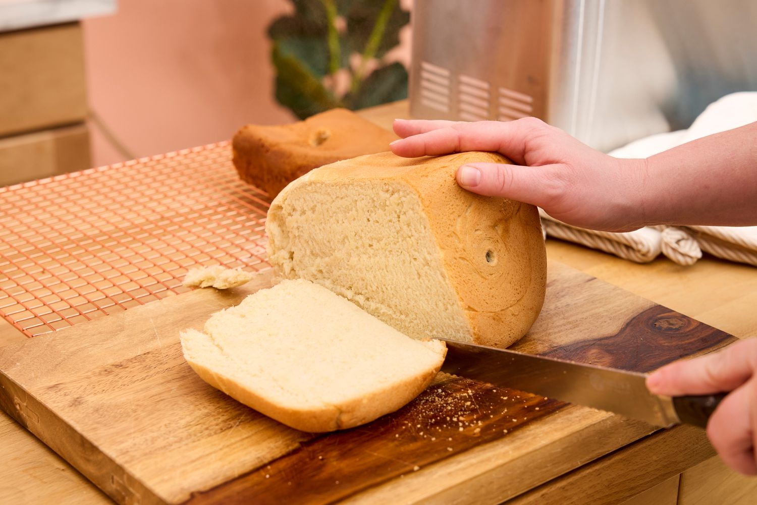 A person cuts into a loaf of bread made in the Amazon Basics 2-Pound Nonstick Bread Making Machine