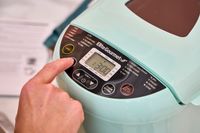 A person presses a button on the Elite Gourmet Programmable Bread Maker