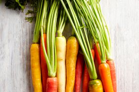 Grouping of rainbow carrots with tops on a white wood board
