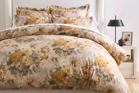 Floralpatterned bedding on a neatly arranged bed with pillows bedside table with lamp and a small framed picture