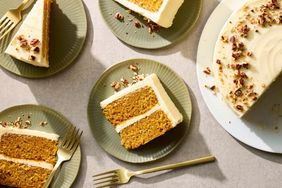 Slices of a twolayer carrot cake on plates with forks topped with frosting and garnished with pecans