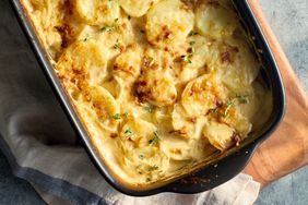 A casserole dish of baked golden sliced potatoes with herbs