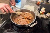 A person cooks meat in the All-Clad D3 3-Ply Stainless Steel Cookware Set pan