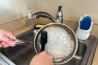 A person washes the Viking Culinary 3-Ply Stainless Steel Cookware Set pan in a sink
