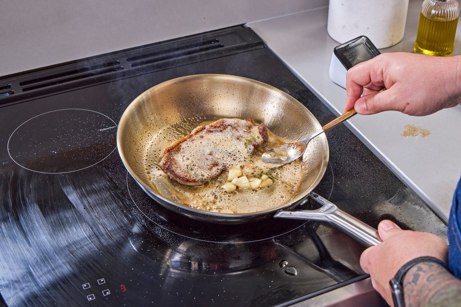 A person cooking a steak in a pan from the Ninja EverClad Commercial-Grade Stainless Steel Cookware 12-Piece Set