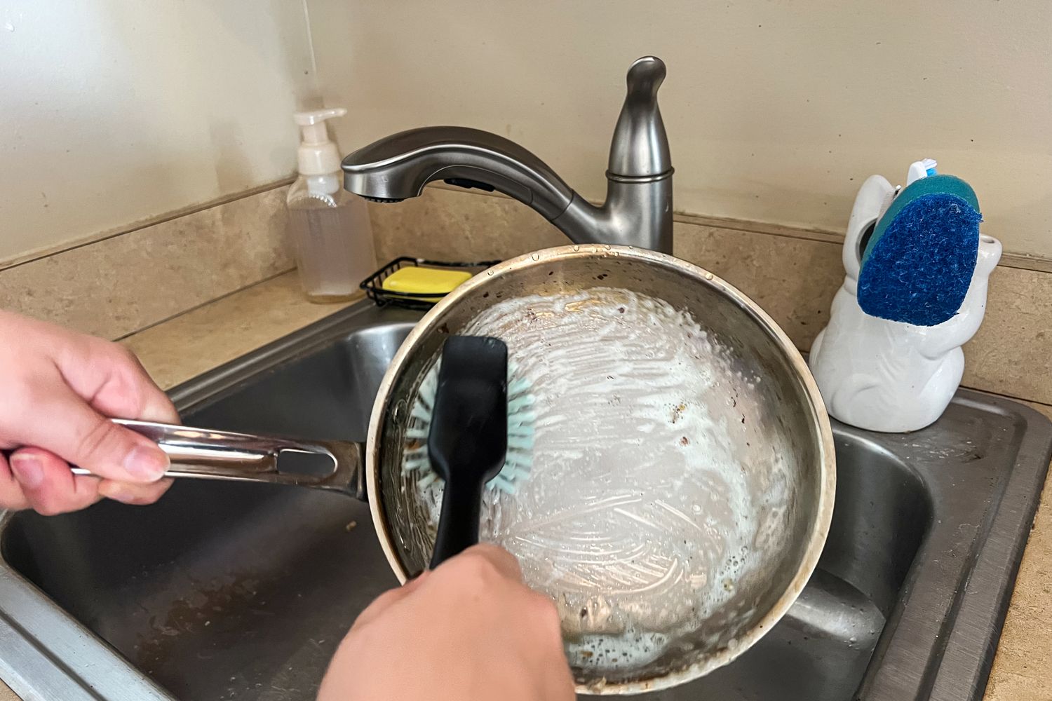 A person washes the Viking Culinary 3-Ply Stainless Steel Cookware Set pan in a sink