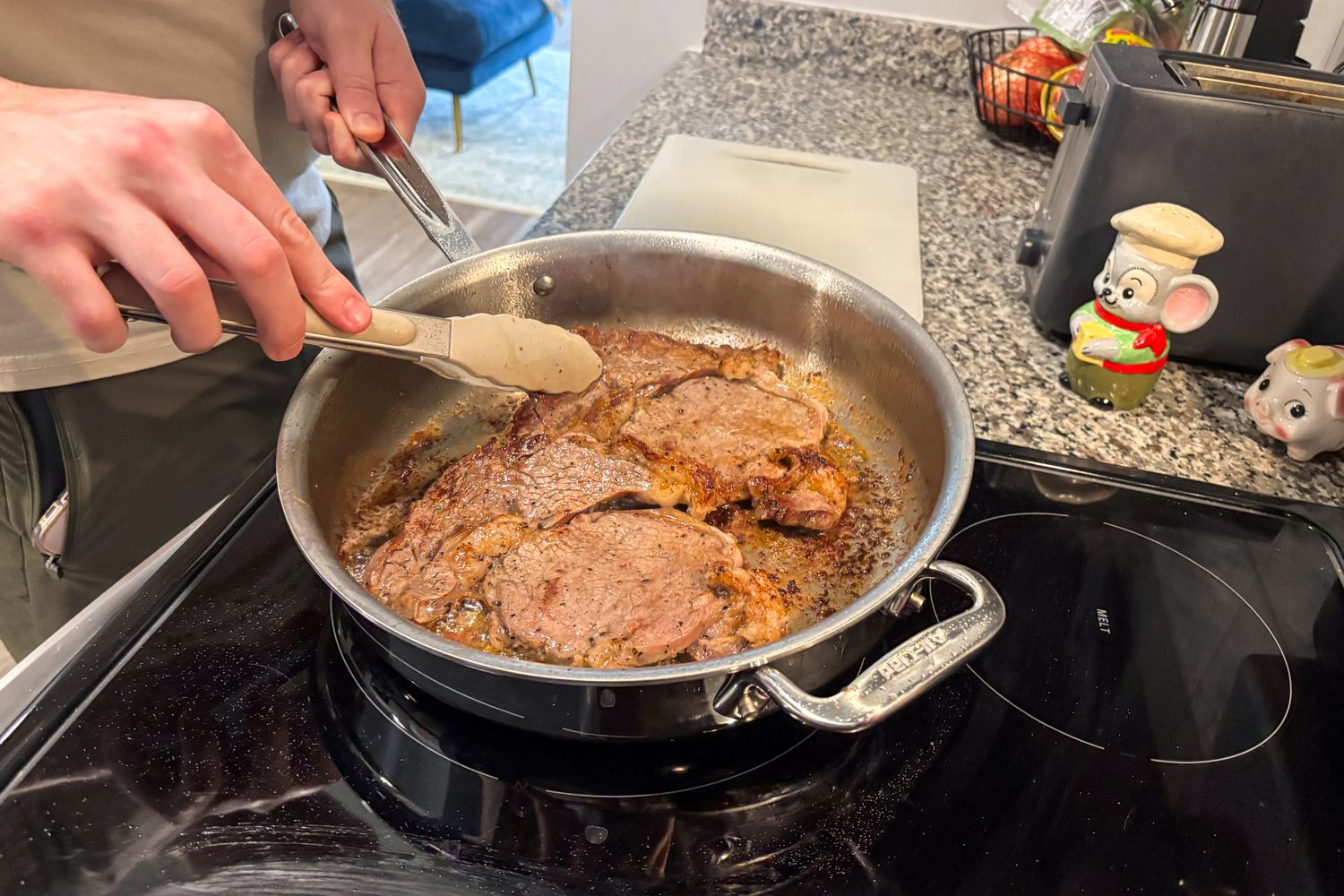 A person cooks meat in the All-Clad D3 3-Ply Stainless Steel Cookware Set pan