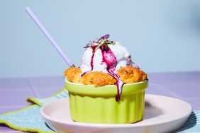 A lavender and blueberry cobbler in a green ramekin with a scoop of ice cream on top, garnished with a straw and flowers