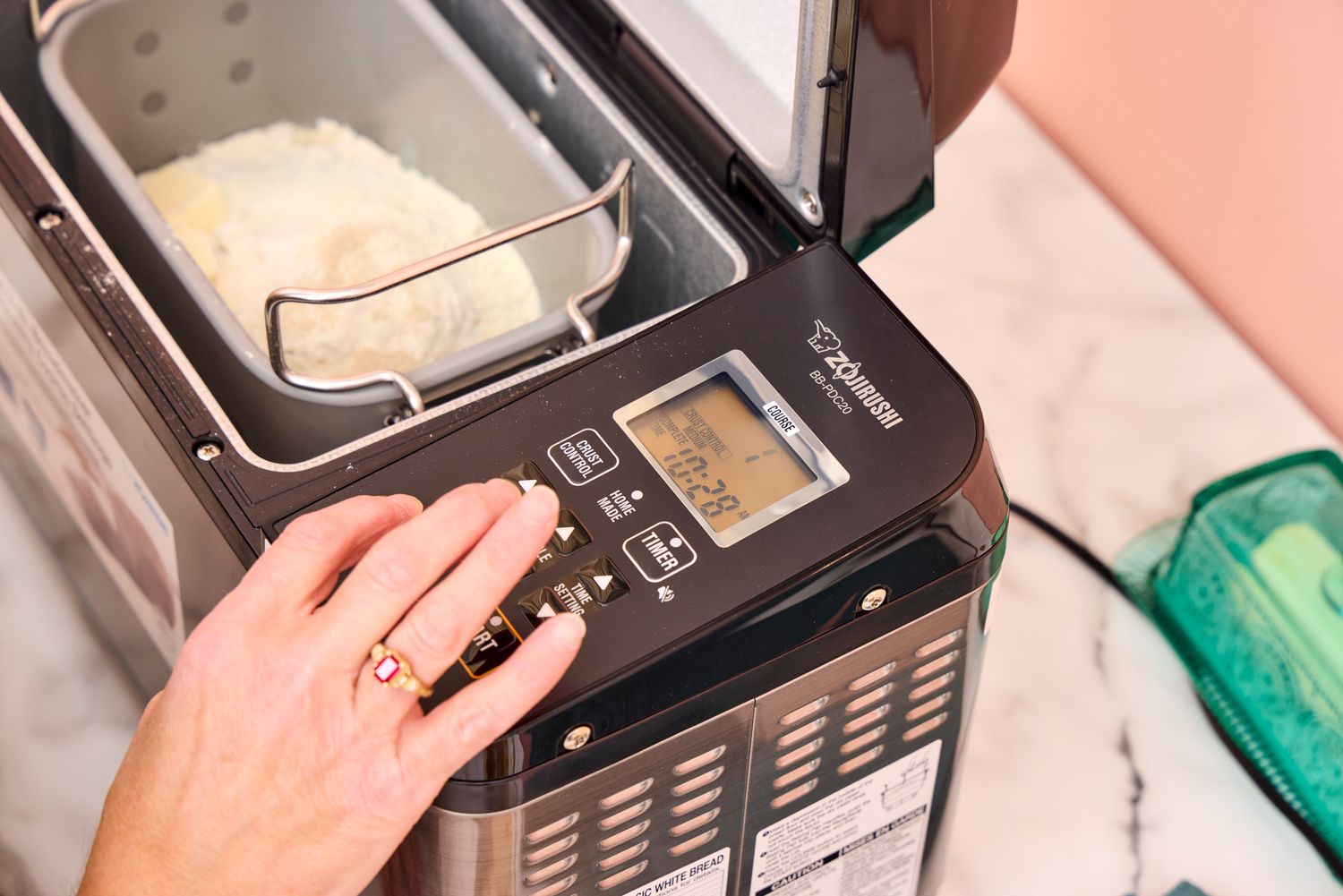 A person presses a button on the Zojirushi Home Bakery Virtuoso Plus Bread Maker