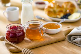 jars and bowls of jams and honey on a wooden cutting board