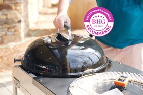 A hand holding the grill top of the Weber Performer Deluxe Charcoal Grill 22"