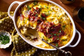 Casserole dish with twicebaked potato casserole topped with bacon and herbs spoon served on the side