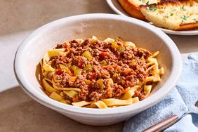 A bowl of goulash with pasta topped with a meat and vegetable sauce served alongside garlic bread