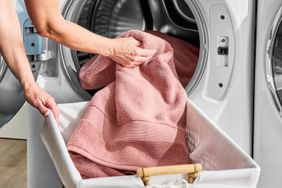 A hand removing a towel from a washing machine into a laundry basket