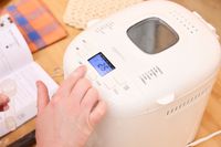 A person presses a button on the Amazon Basics 2-Pound Nonstick Bread Making Machine