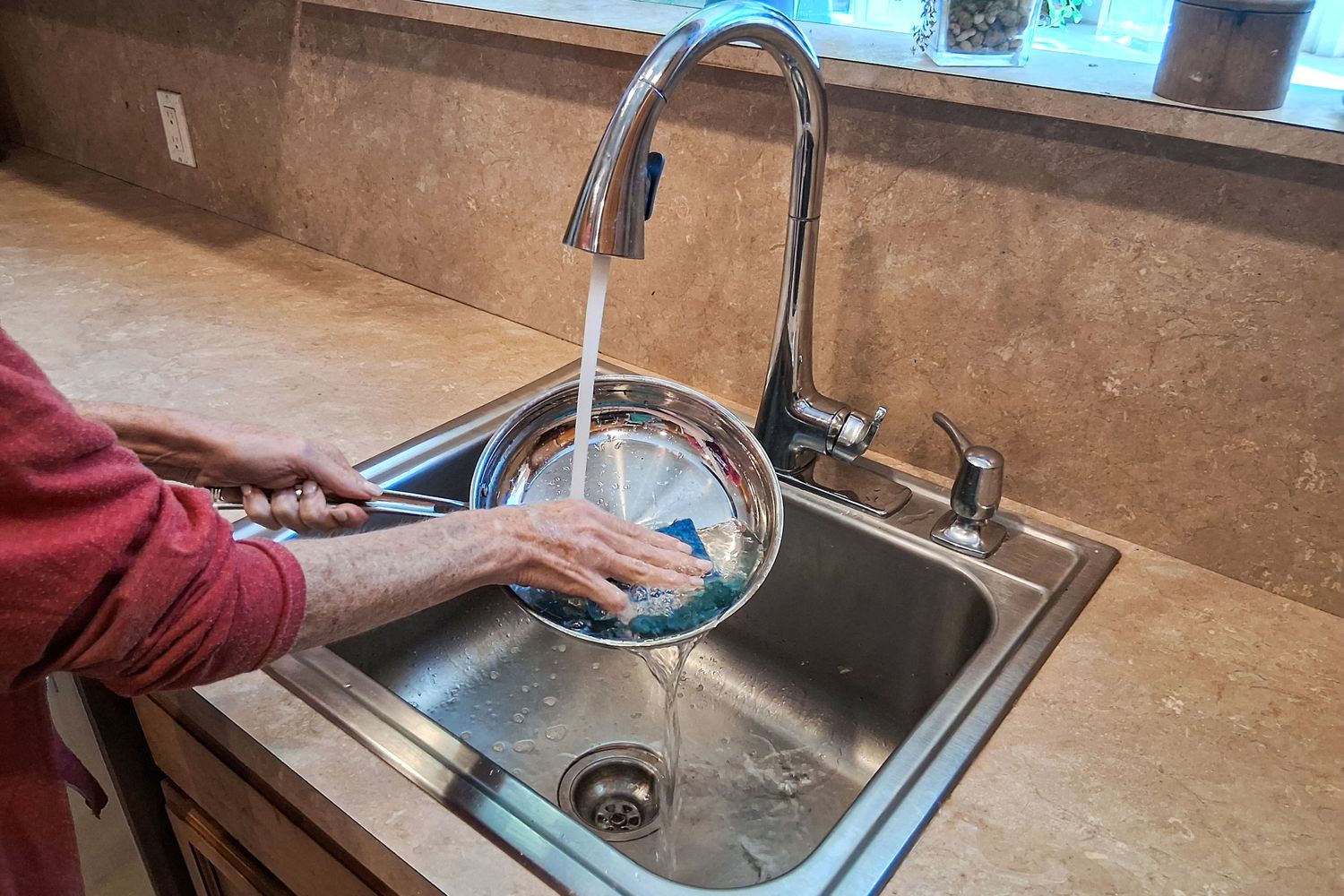 A person washes the Cuisinart MultiClad Pro 12 Piece Stainless Cookware Set pan in a sink