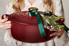 Person holding a large pot adorned with greenery tied by a ribbon