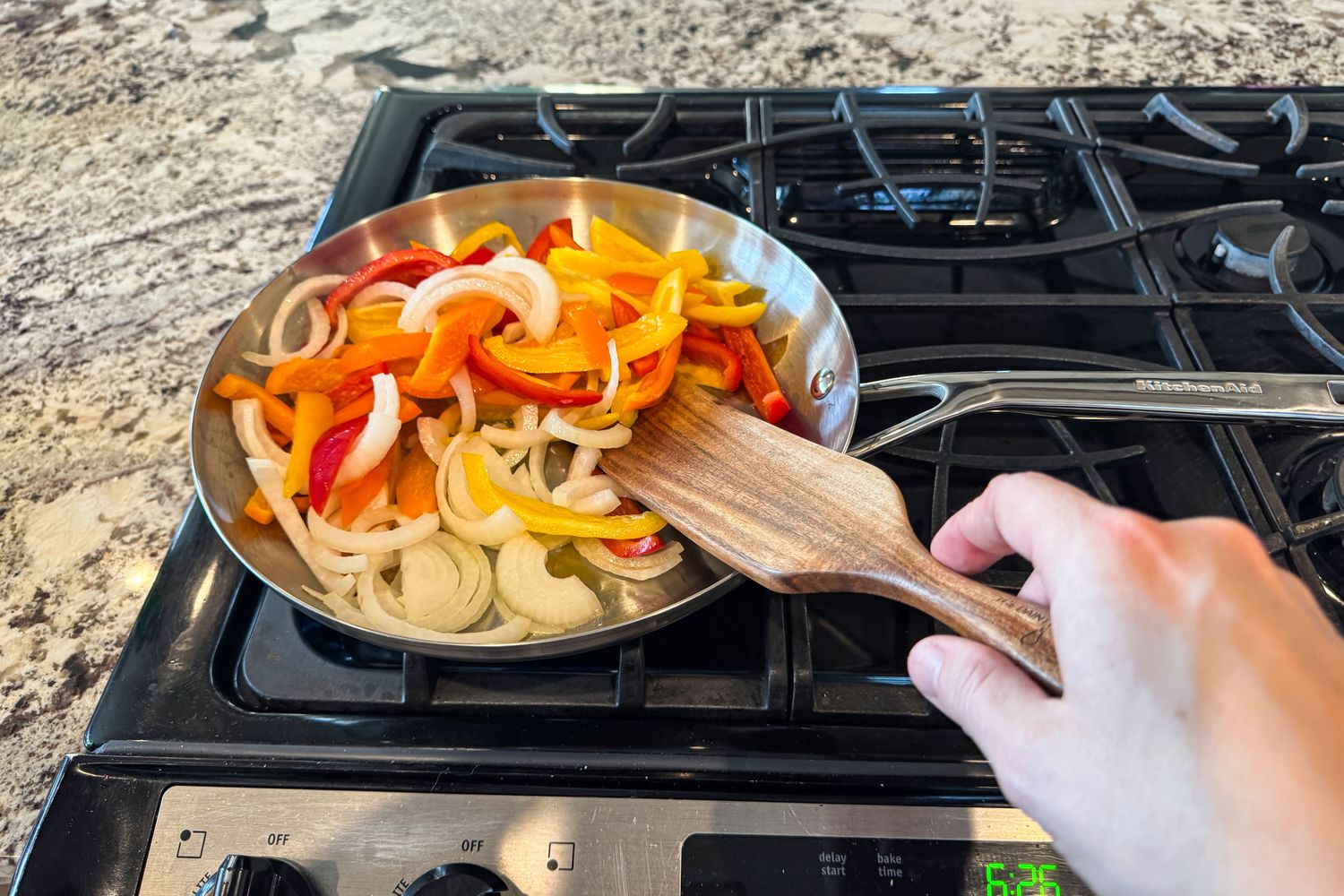 A person cooks peppers and onions in a KitchenAid 11 Piece 3-Ply Stainless Steel Cookware Set pan