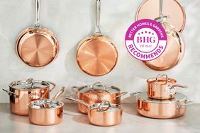A variety of copper cookware sets on a table and handle from hooks in a kitchen setting